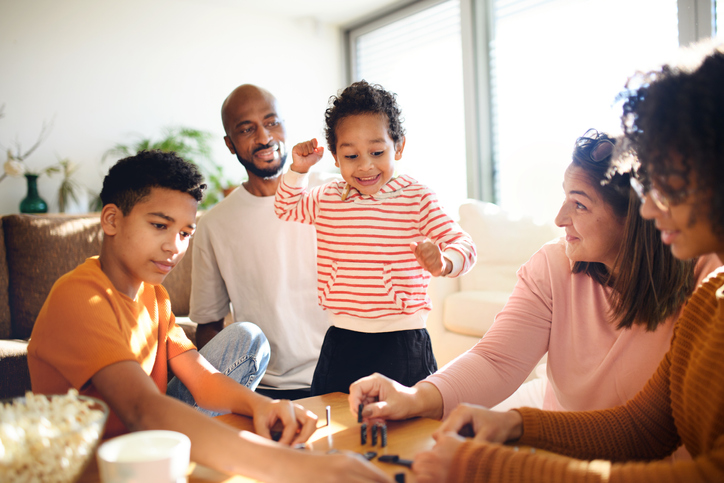 Happy multiracial family with three children playing domino at home.