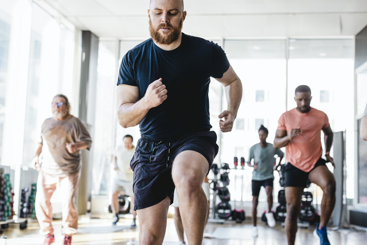 Determined man practicing jogging with male friends during exercise class in gym